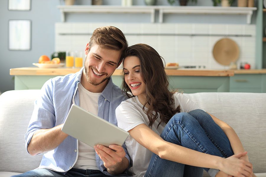 Insurance Quote - Young Couple Sitting On Couch In Apartment Using Tablet